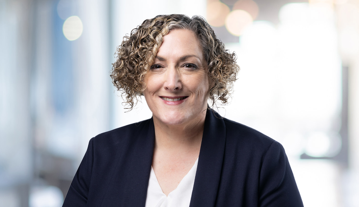 Photo of our Chief Customer Advocate - Teresa Corbin. Teresa has short curly blonde hair, is wearing a dark blue blazer, and is seated in front of a white background.