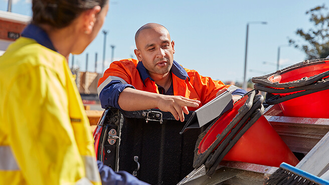 A man in an orange work shirt reading a clipboard in a truck with road cones.