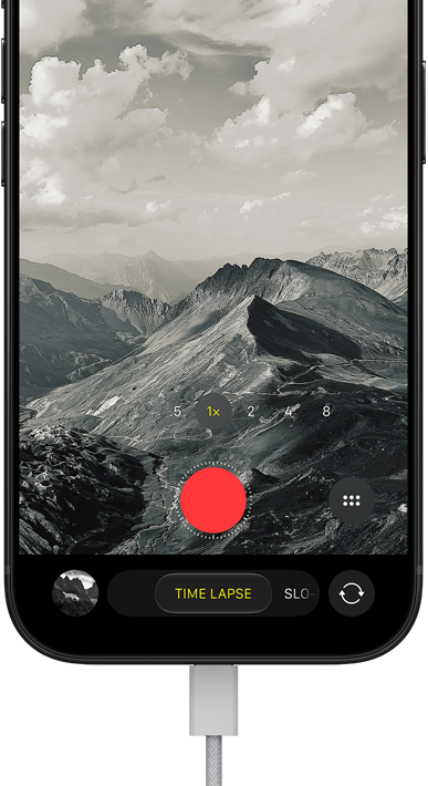iPhone 18 Pro, front exterior, displaying a mountainous landscape, with the camera mode overlay in Time-Lapse mode, with power cable attached to charging port