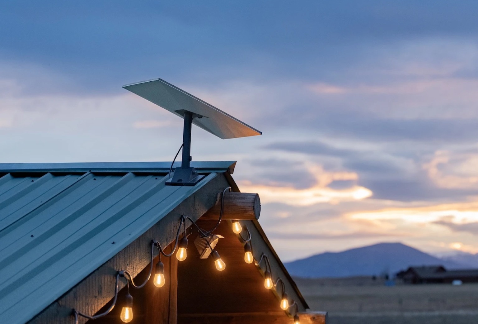 Rooftop Starlink antenna overlooking  an open landscape and distant mountain  silhouettes at sunset.