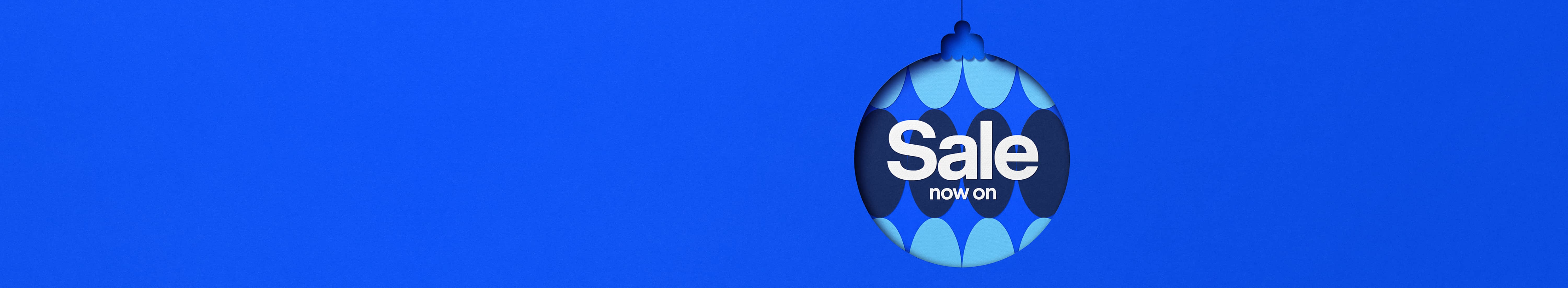 Blue Christmas bauble with white text saying ‘Sale now on’ against a patterned blue background.