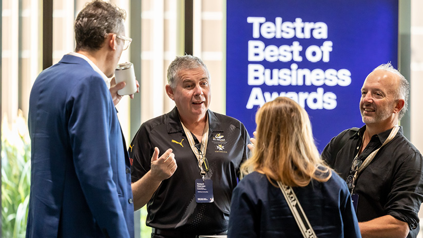A small group of people engaged in a group discussion in front of a Telstra Best of Business Awards sign.