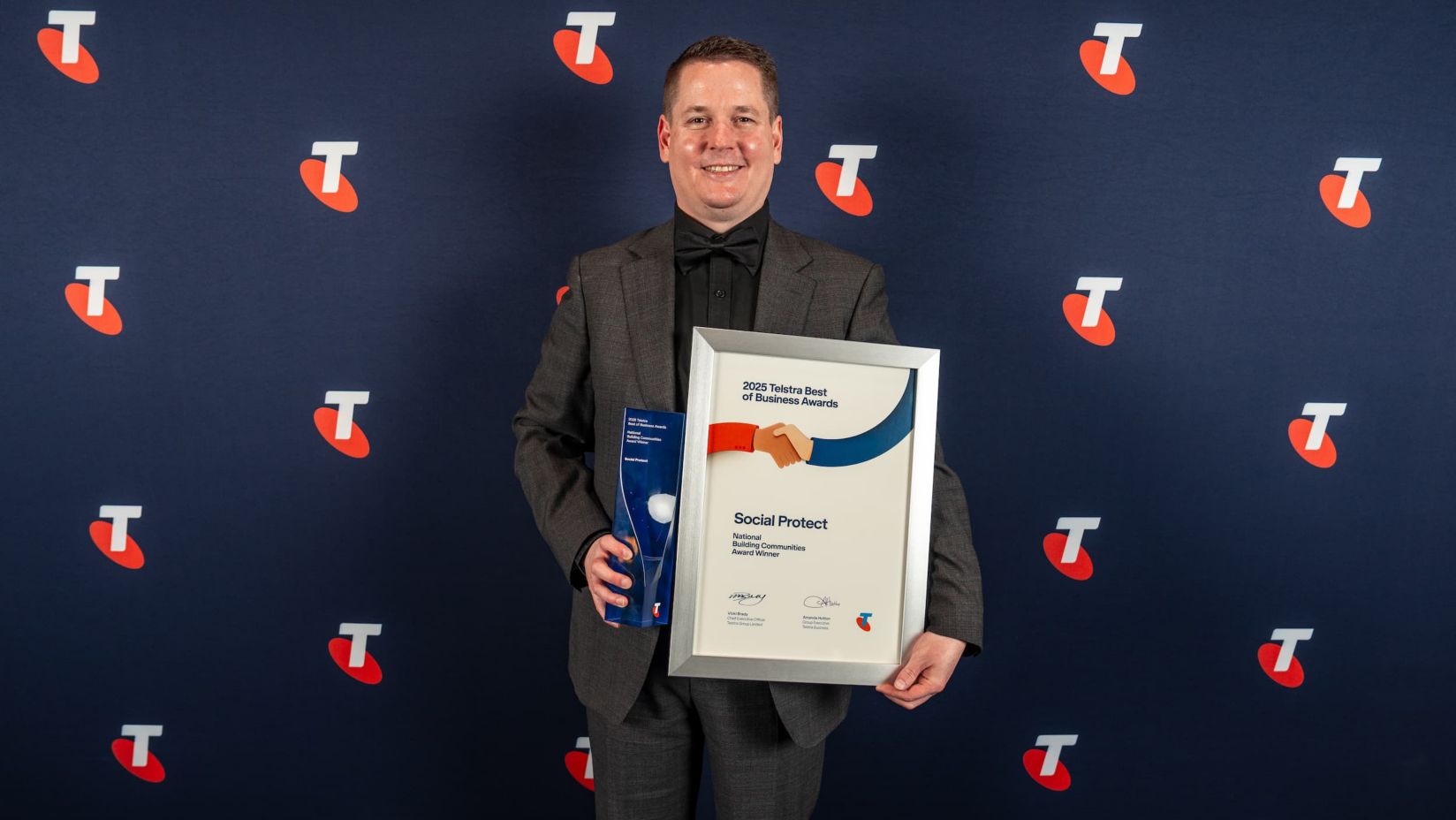 Shane is smiling and holding Social Protect’s award and award certificate.