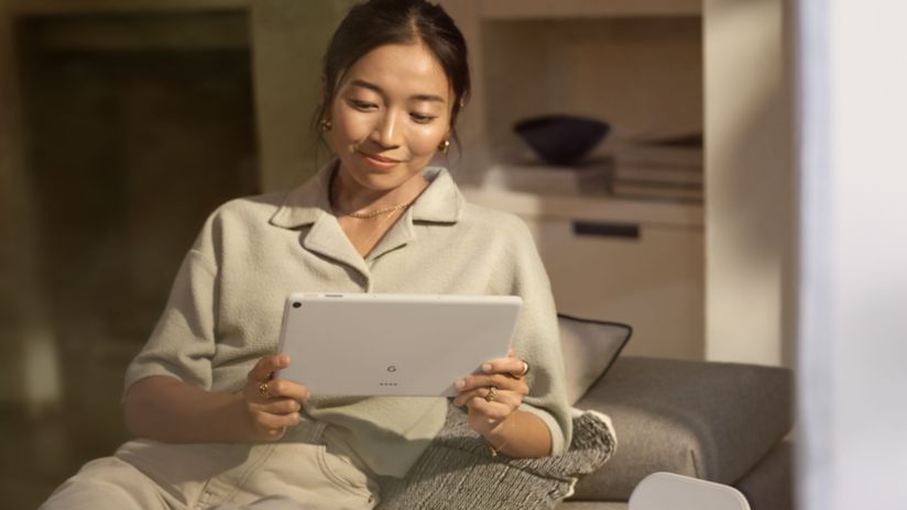 A woman sitting on a couch holding the new Google Pixel Tablet