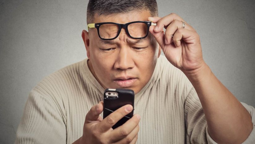 A man looking at his smartphone over his glasses.