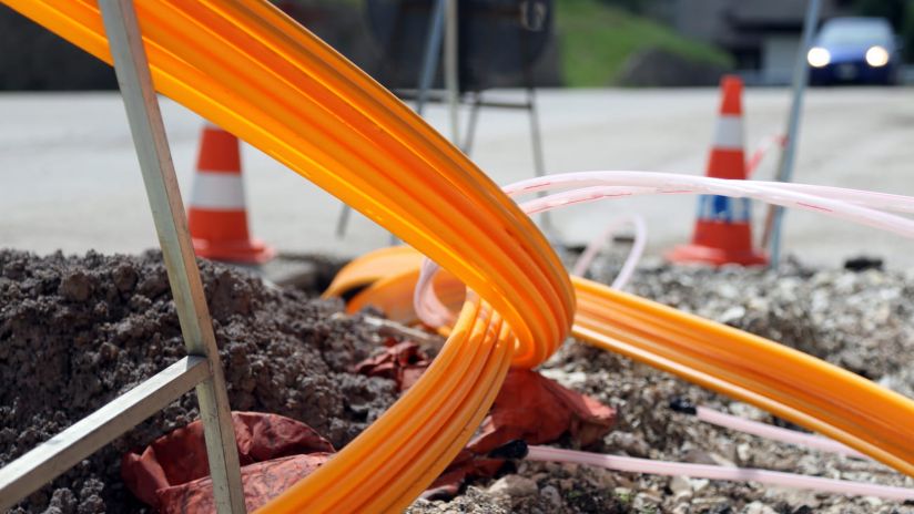 Two spools of fibre optic cable are carried by heavy construction equipment.