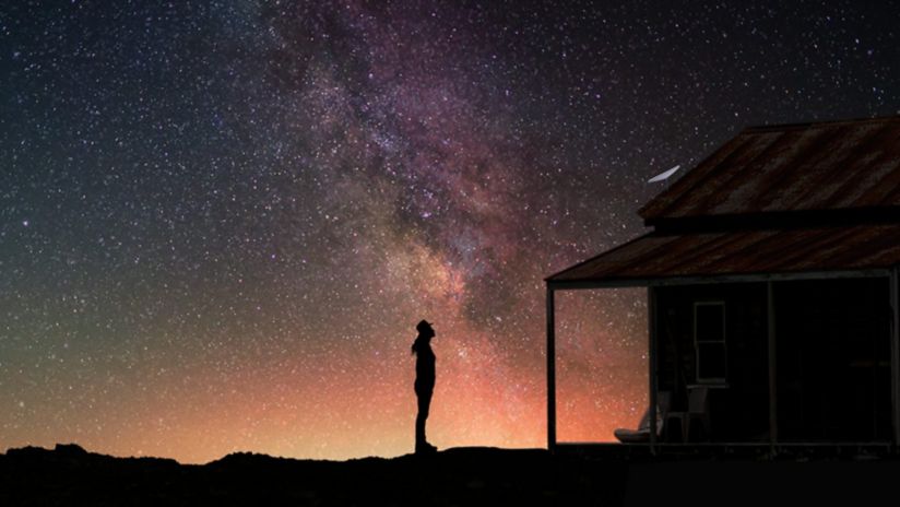 A person looking up at a night sky scene standing in front of a house.