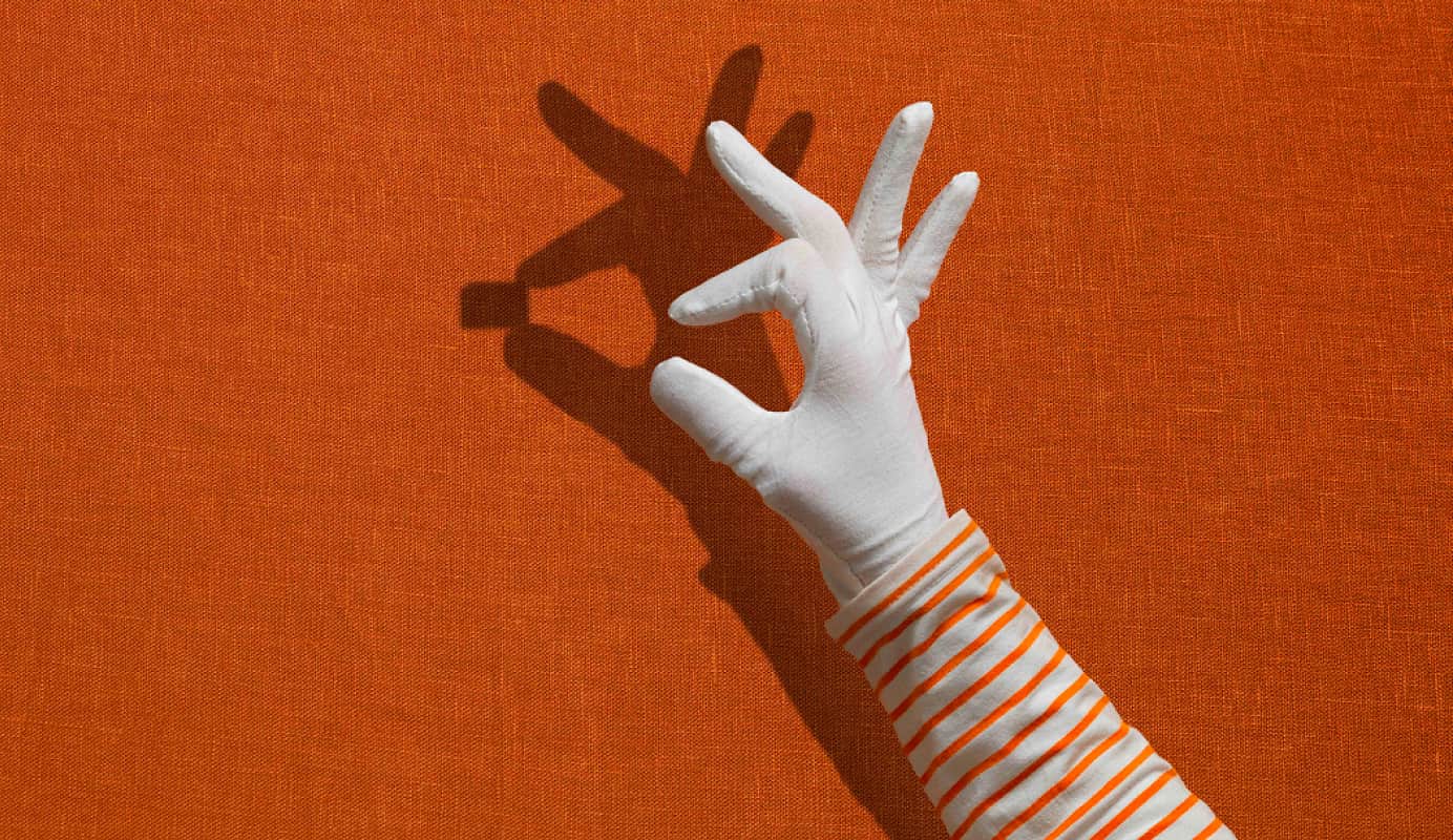 The hand of a mime with white gloves with a space between their index finger and thumb. In the shadow behind the hand this space is filled with a SIM card.