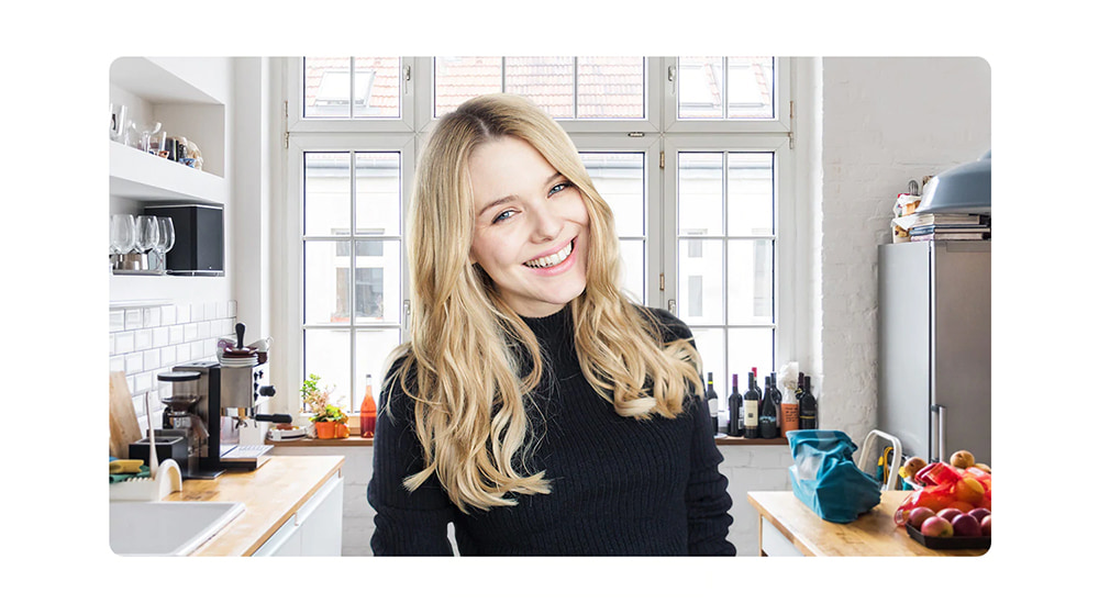 A young, blond smiling woman in her kitchen.